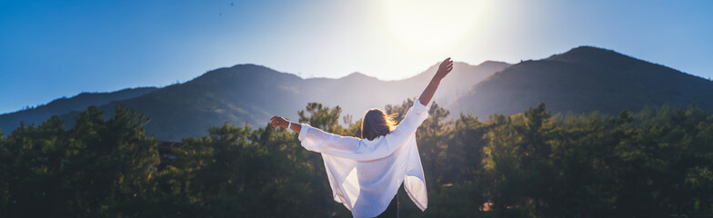 A person standing outdoors with arms raised toward the mountains at sunrise